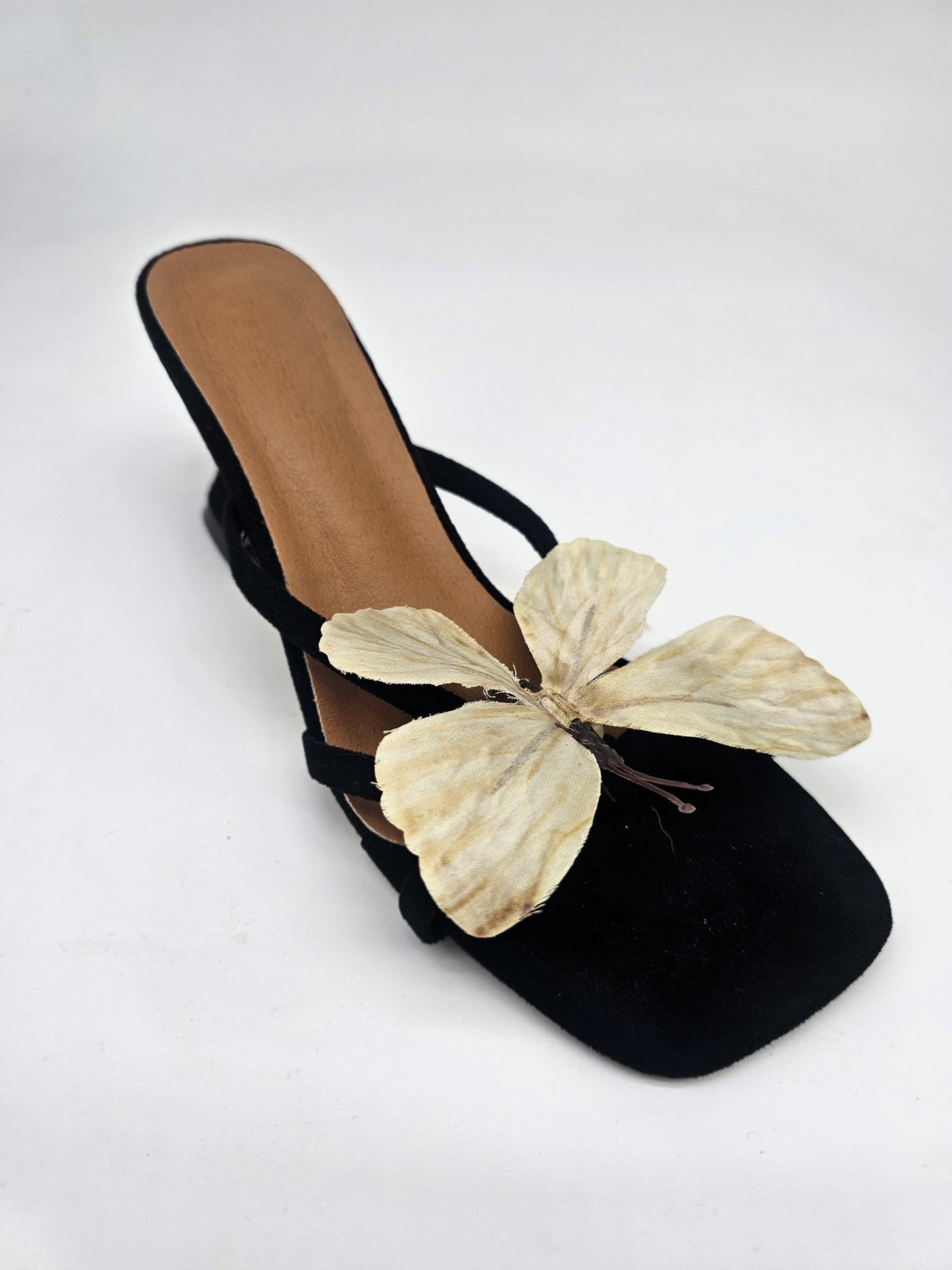 Black heeled sandals with cushioned sole and handcrafted beige butterfly detail, comfortable women’s heels for casual and formal wear.