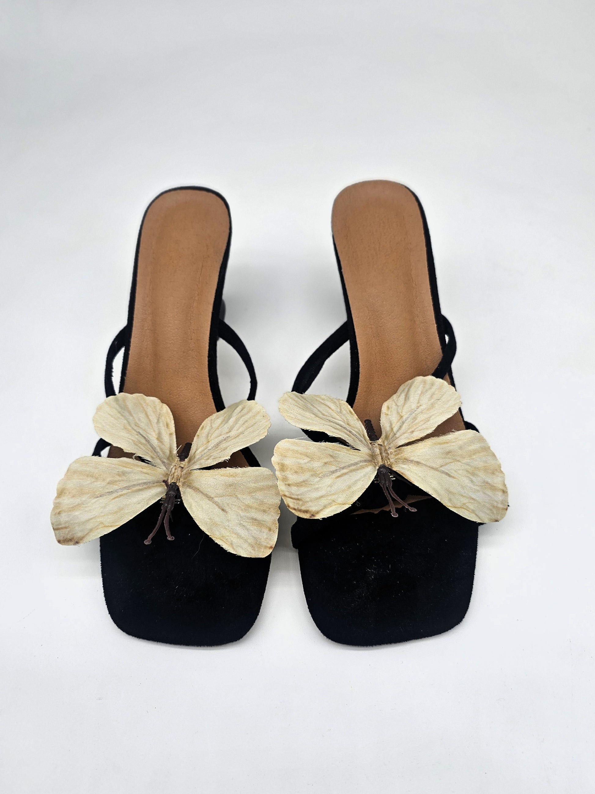 Black heeled sandals with cushioned sole and handcrafted beige butterfly detail, comfortable women’s heels for casual and formal wear.