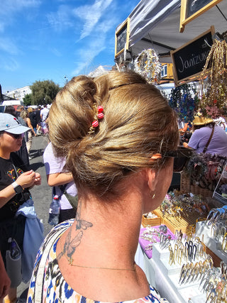 A woman at an outdoor market wearing a blonde half-updo hairstyle with a red french comb
