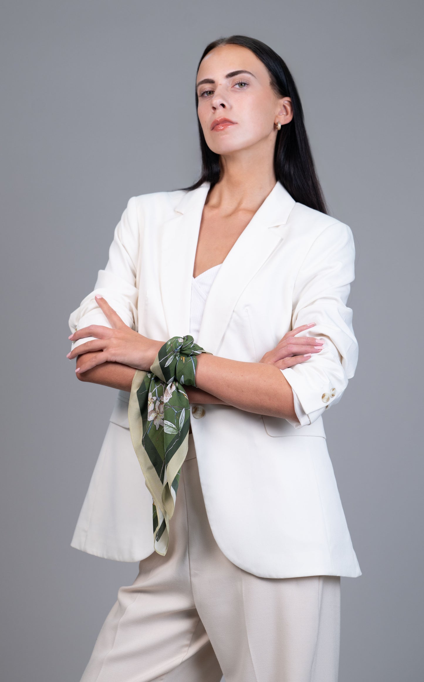 Model wearing a 55×55 cm green botanical 100% mulberry silk square scarf tied as a wrist wrap with a white blazer.
