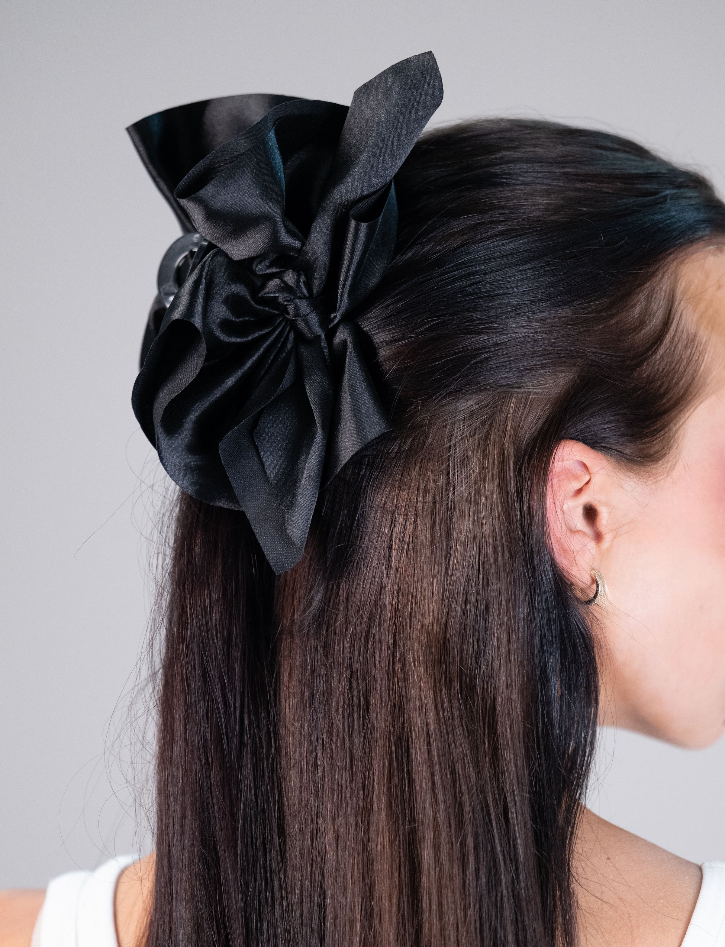 Model wearing an oversized black satin hair bow clip in a half-up hairstyle